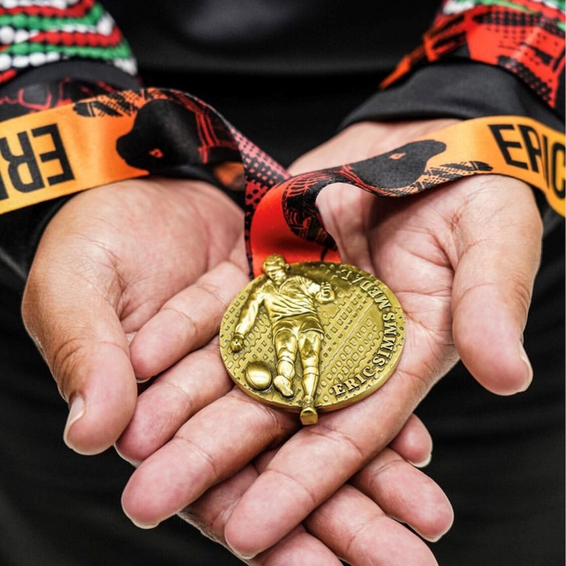 Gold football medal held in hands with colourful ribbon